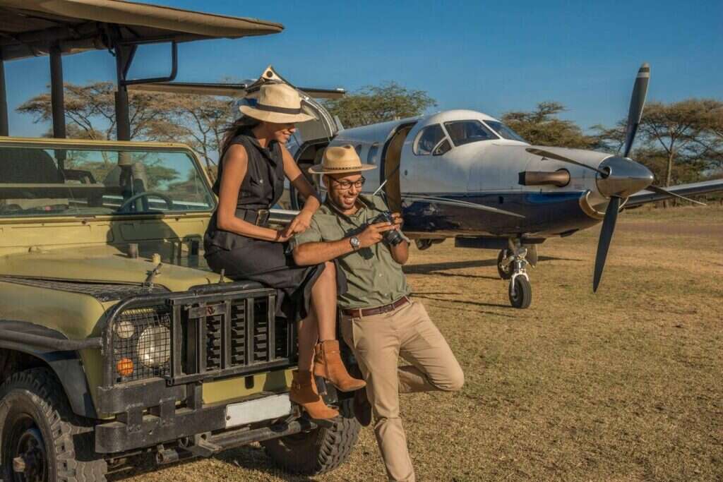 Two travellers beside a safari vehicle and a small aircraft
